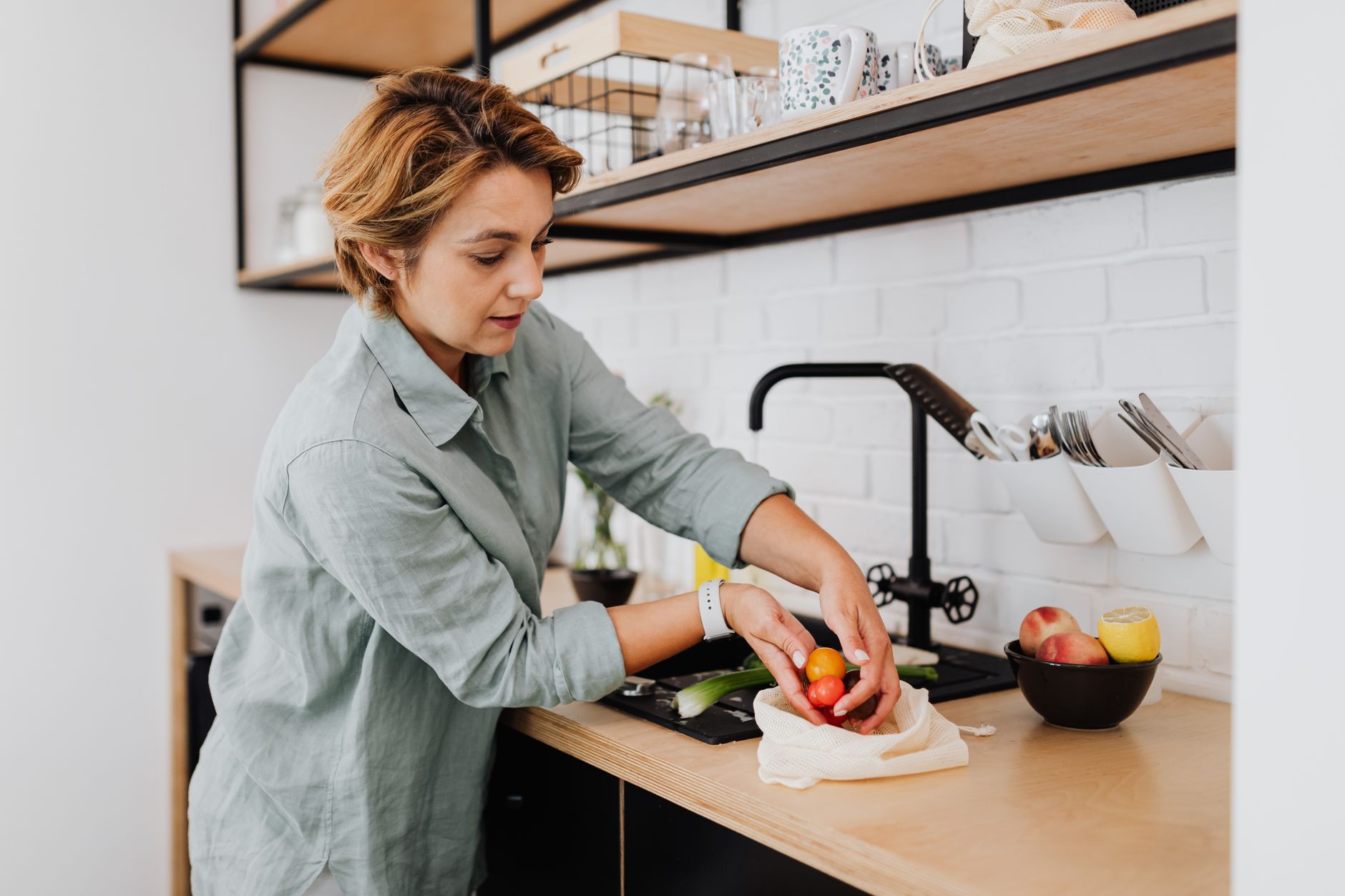Femme d'une quarantaine d'années préparant des légumes frais dans une cuisine lumineuse