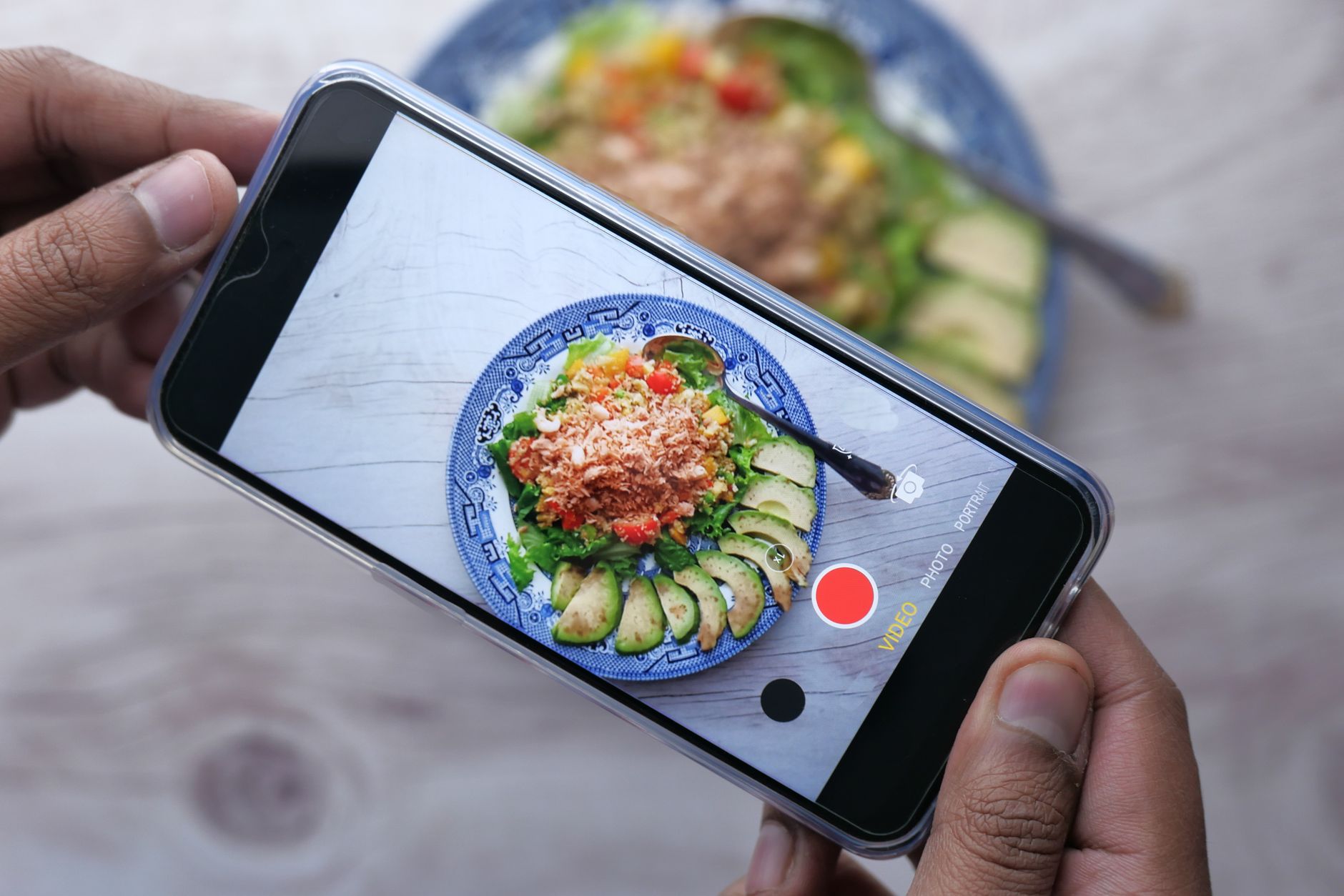 Mains tenant un smartphone en train de photographier une assiette colorée de salade et avocat