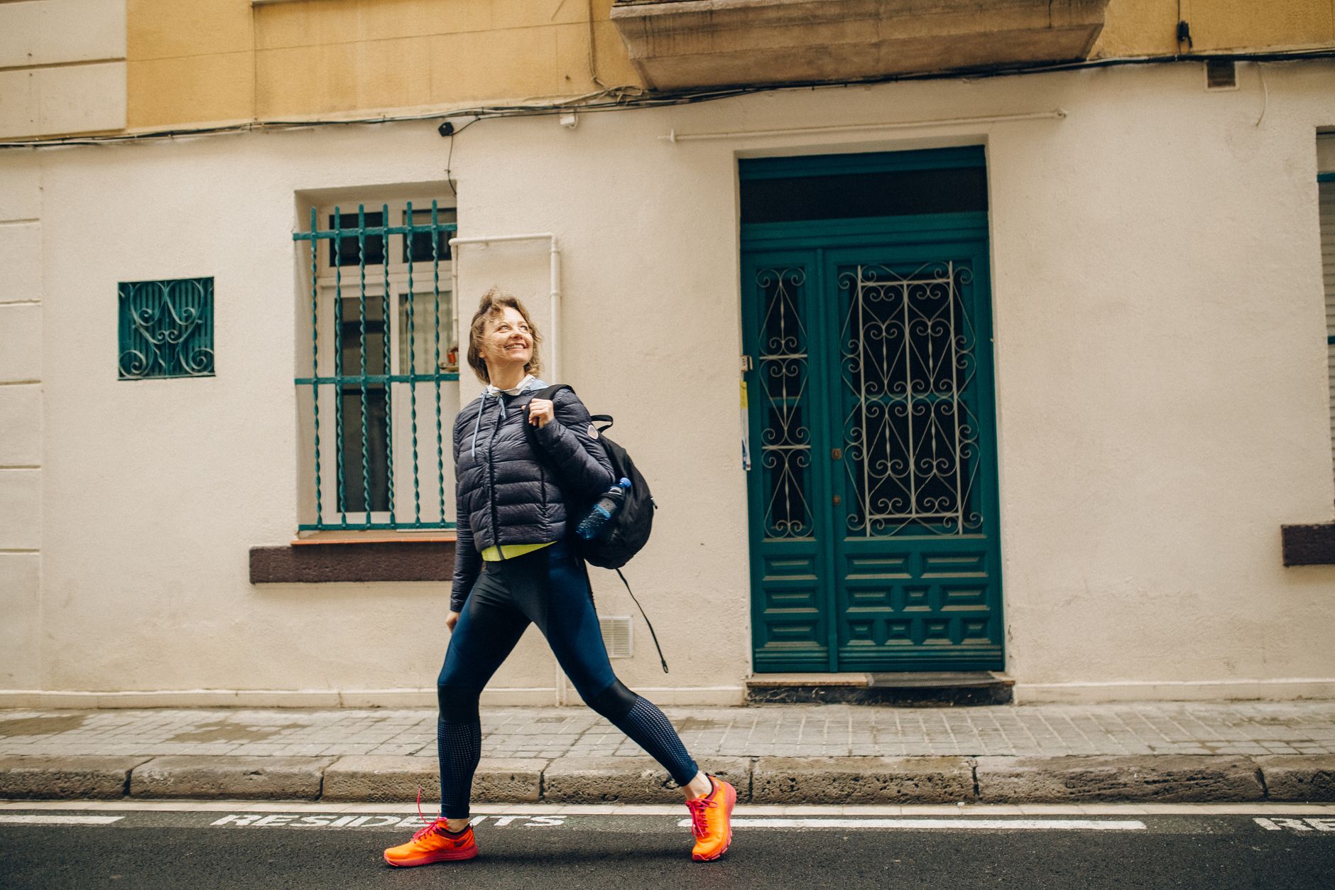 Femme souriante marchant d'un bon pas dans une rue ensoleillée, sac sur l'épaule