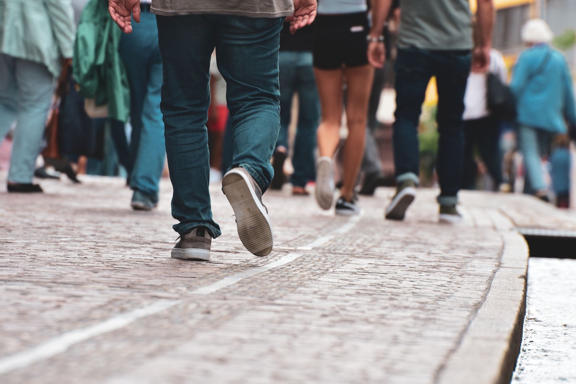Groupe de personnes marchant sur un trottoir pavé en centre-ville, jambes et chaussures en mouvement