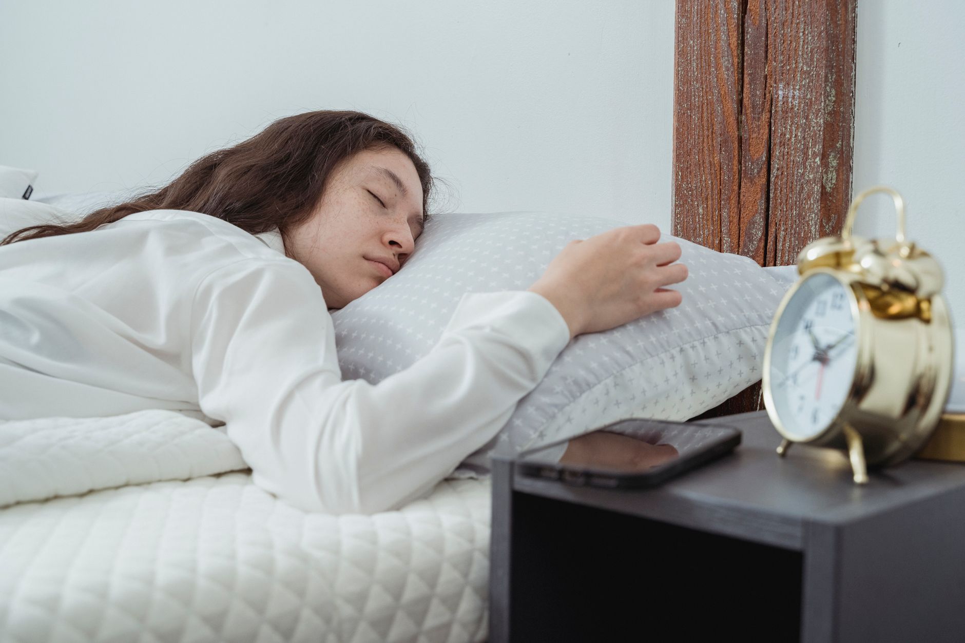 Jeune femme endormie paisiblement dans son lit, avec un réveil doré posé sur la table de chevet