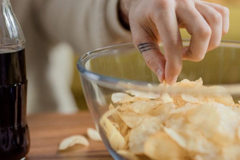 Main attrapant des chips dans un bol, à côté d'une boisson