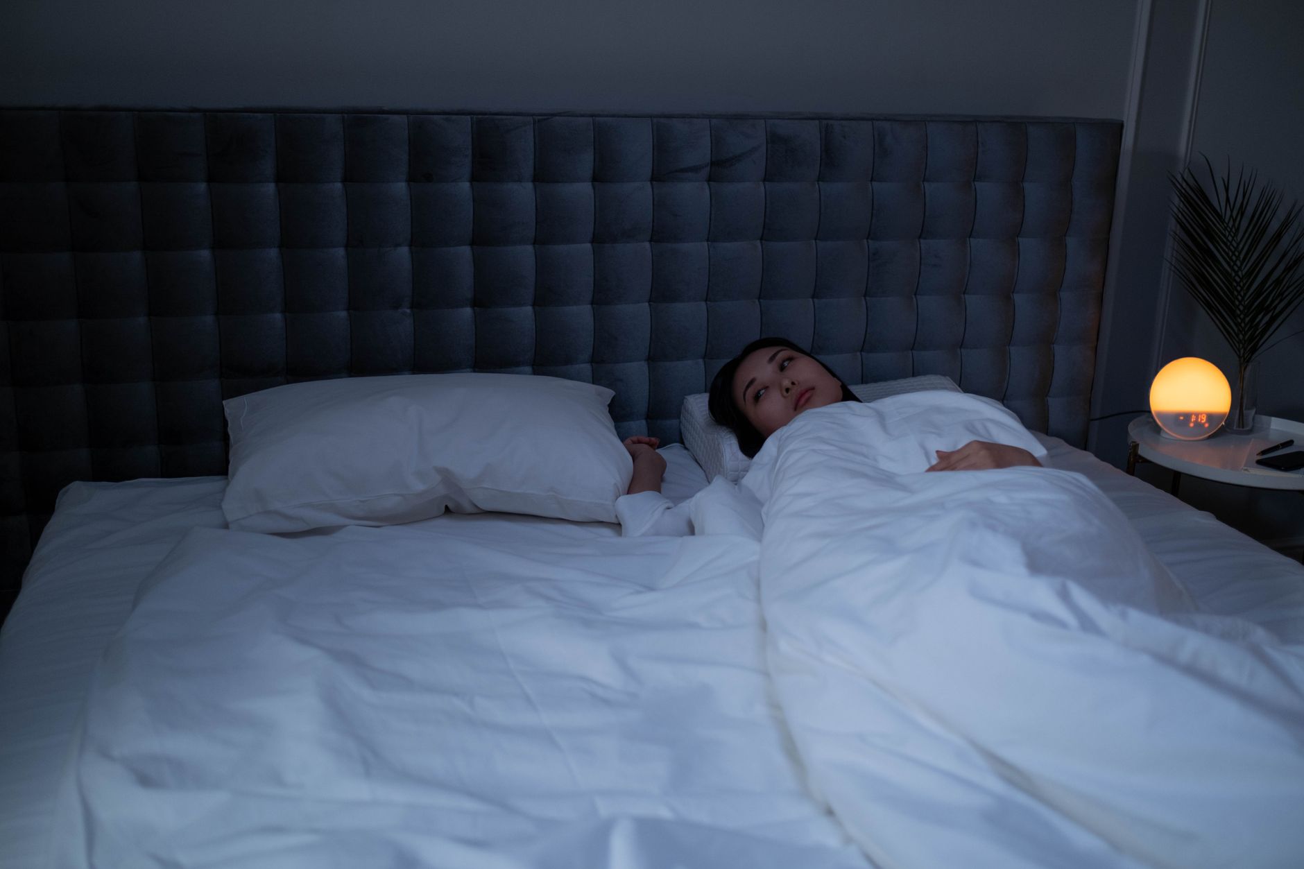 Femme allongée éveillée dans son lit la nuit, dans une chambre faiblement éclairée par une petite lampe chaude