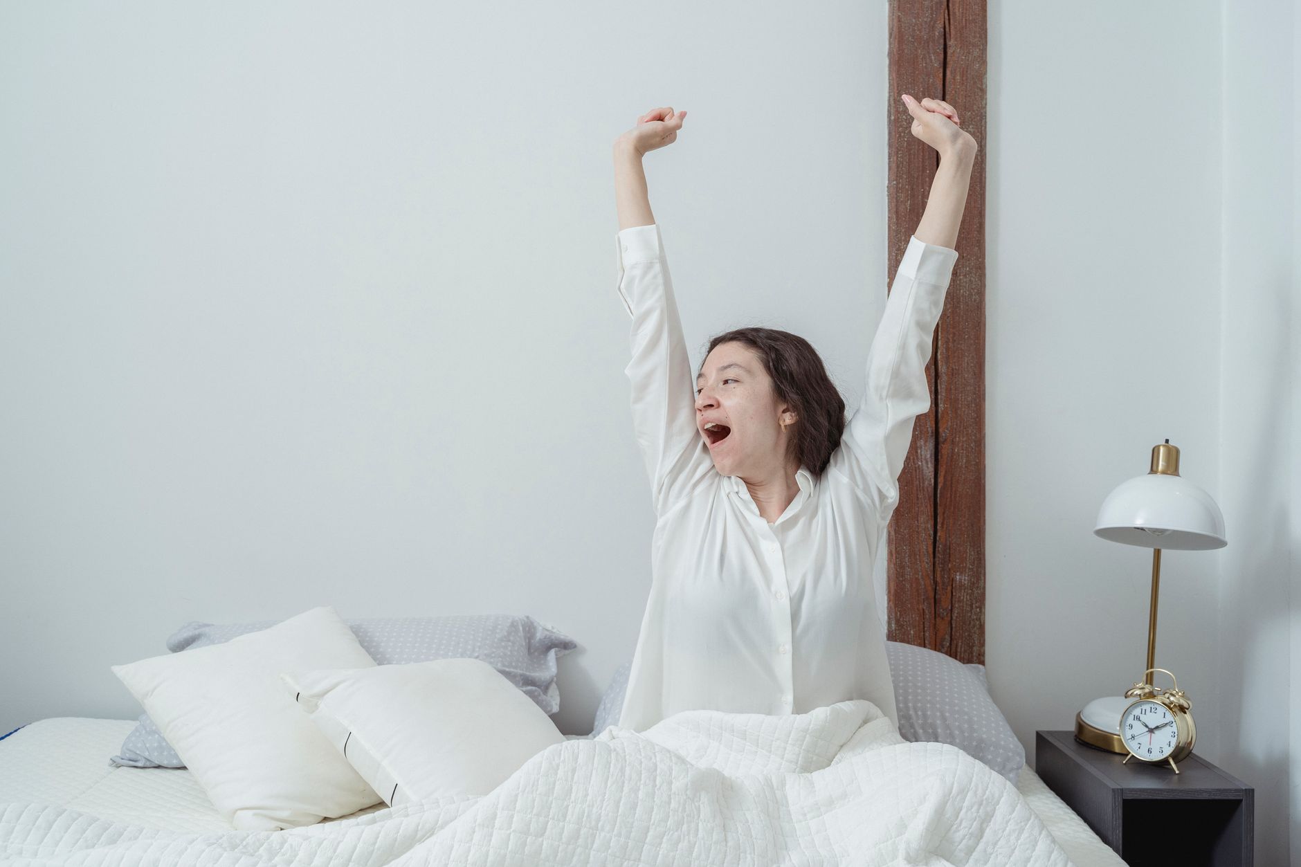 Jeune femme s'étirant en s'éveillant dans un lit lumineux, après une nuit de sommeil