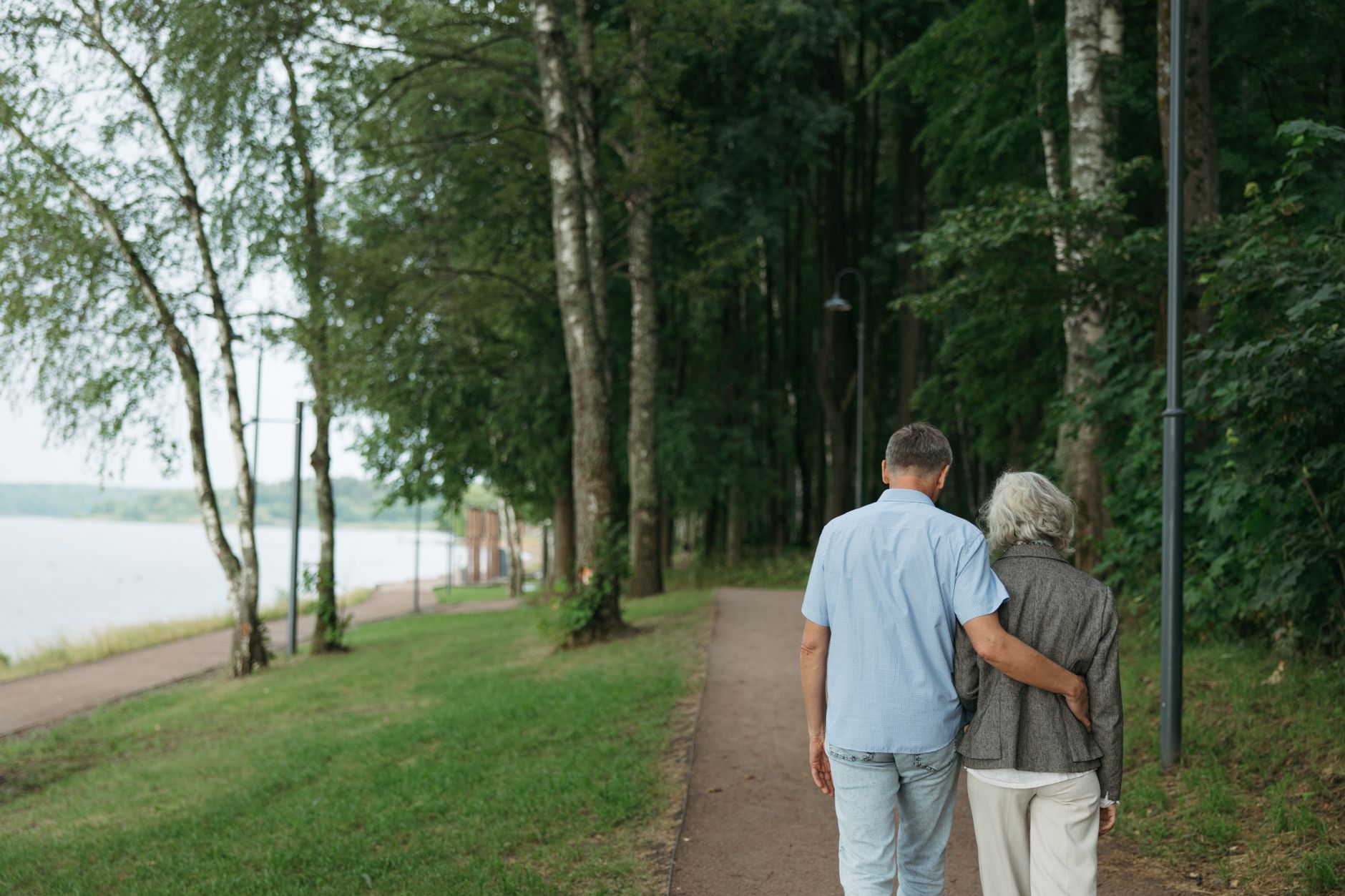 Couple marchant tranquillement bras dessus bras dessous le long d'un chemin en bord de lac, le soir