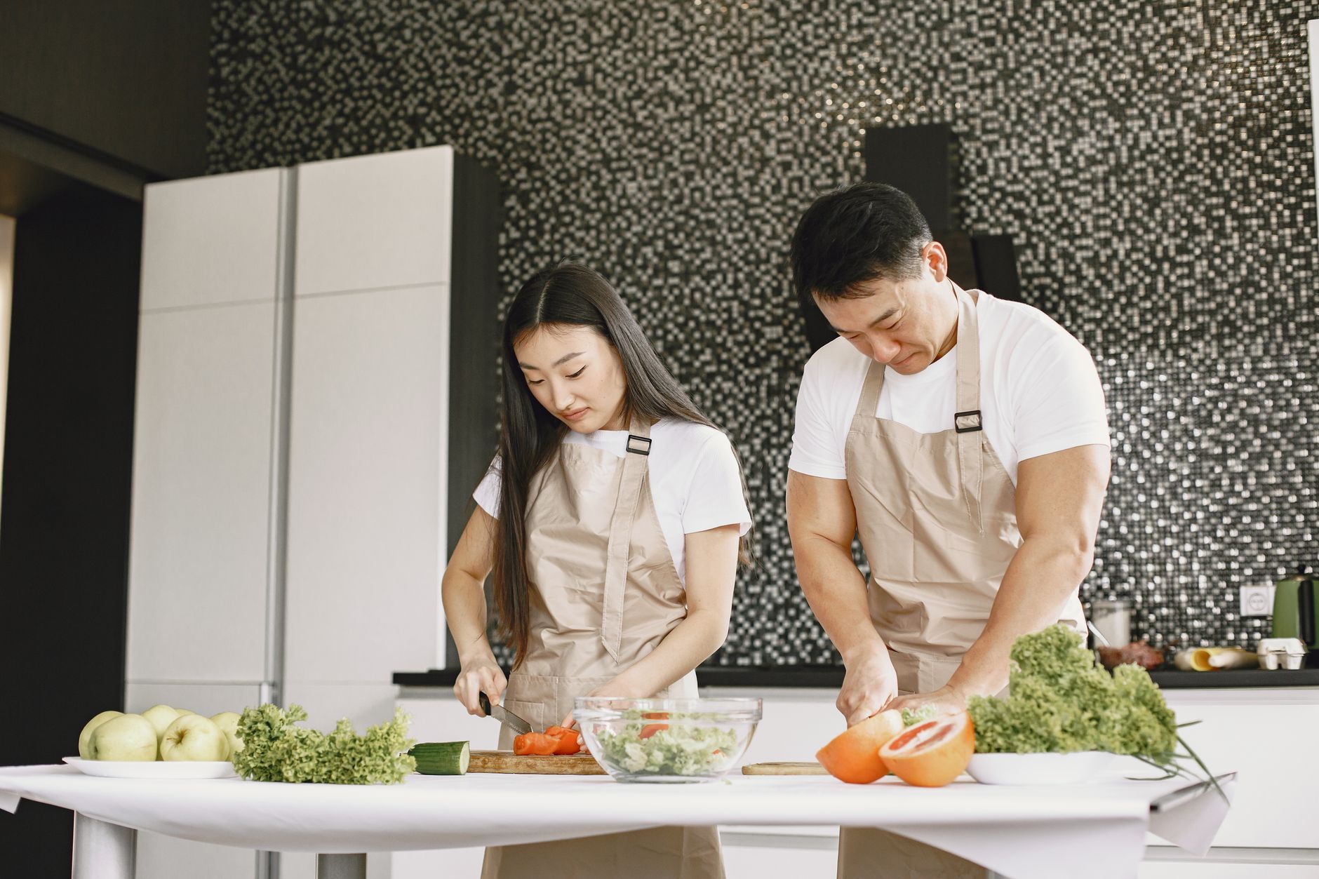 Couple préparant un repas sain ensemble dans une cuisine moderne et lumineuse, en train de couper des légumes