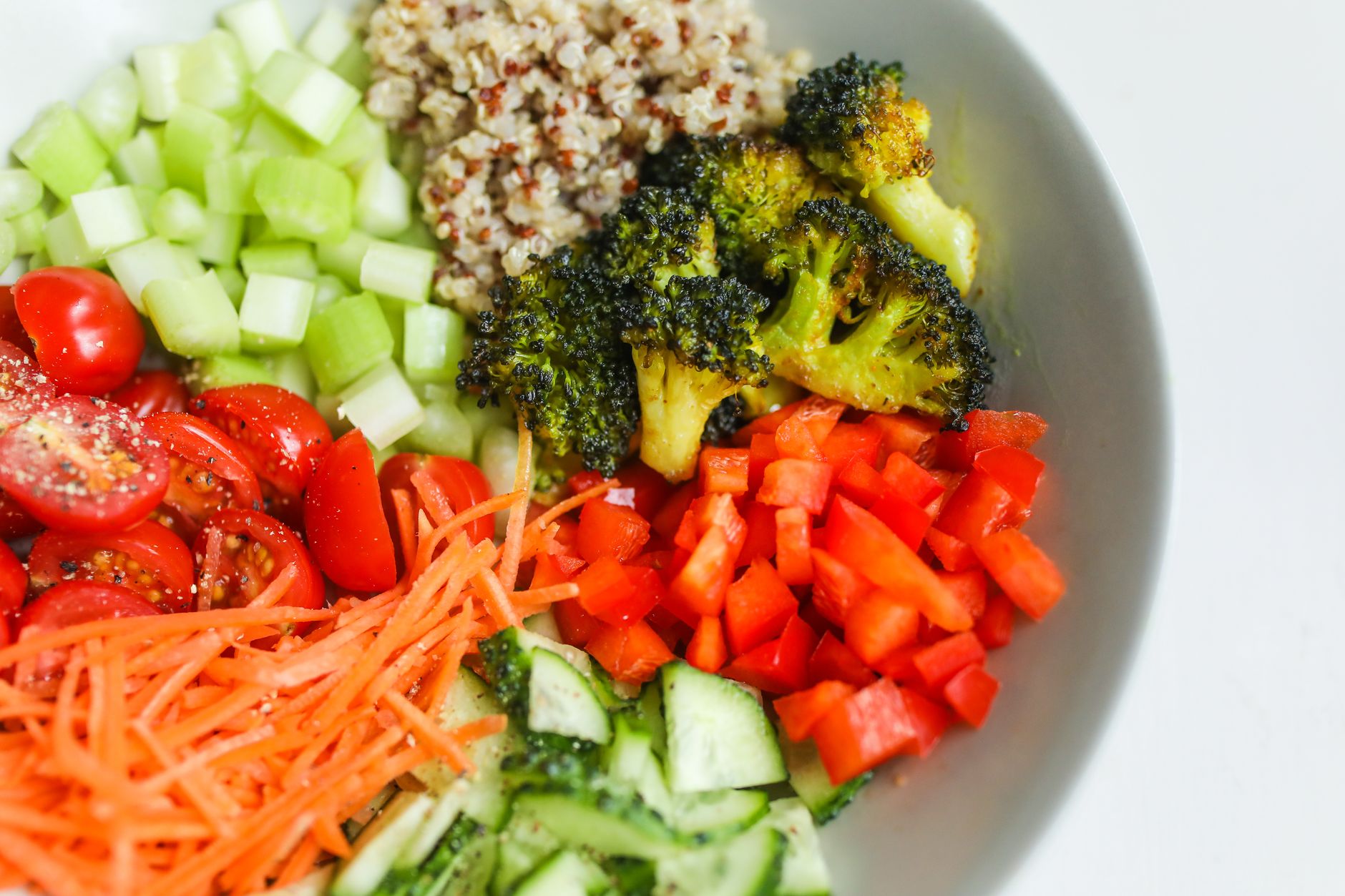 Bol composé de quinoa, brocolis, tomates cerises, carottes râpées, concombre et poivrons pour une assiette équilibrée