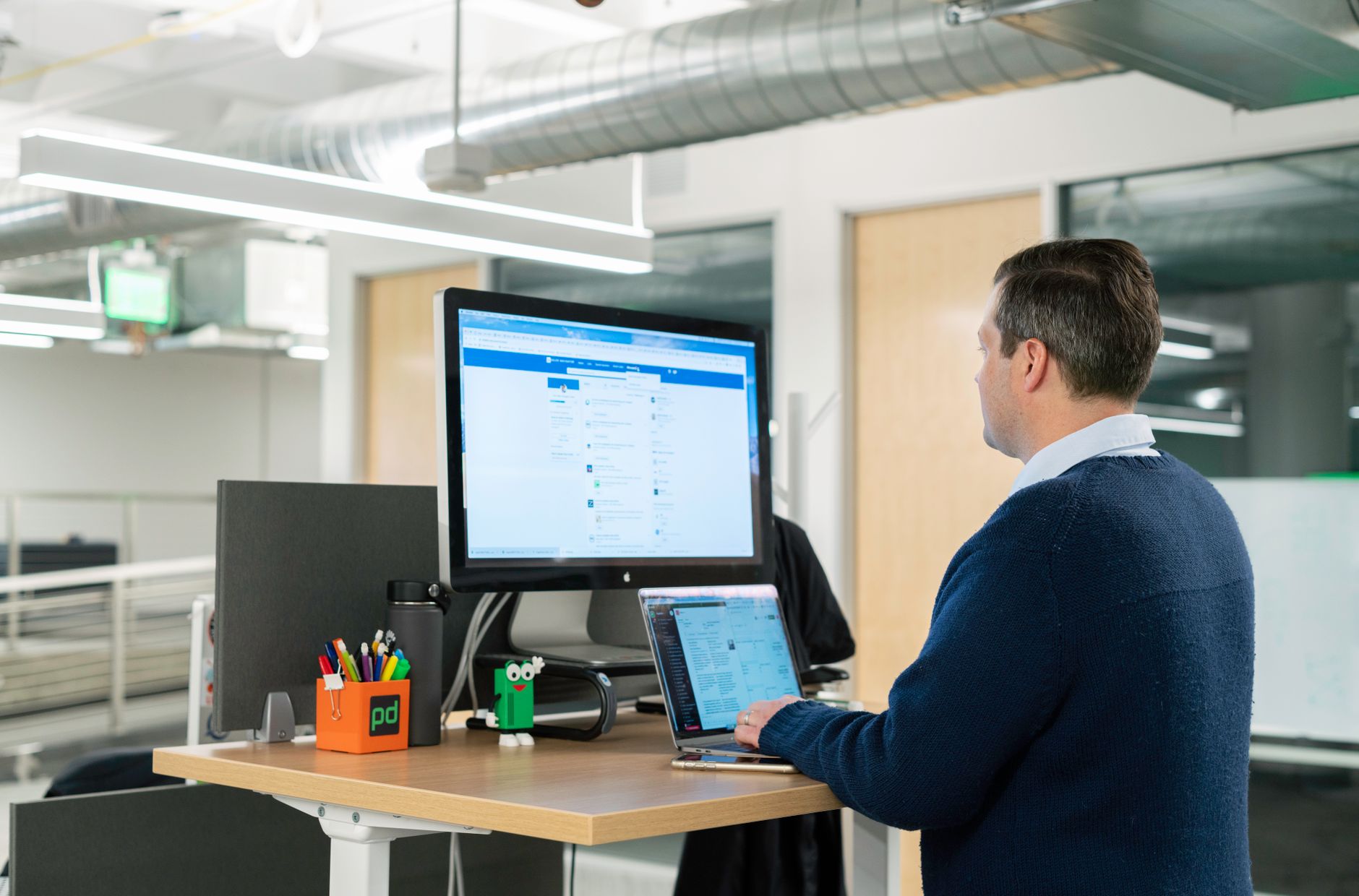 Homme travaillant debout à un bureau haut, ordinateur portable en main, dans un bureau lumineux