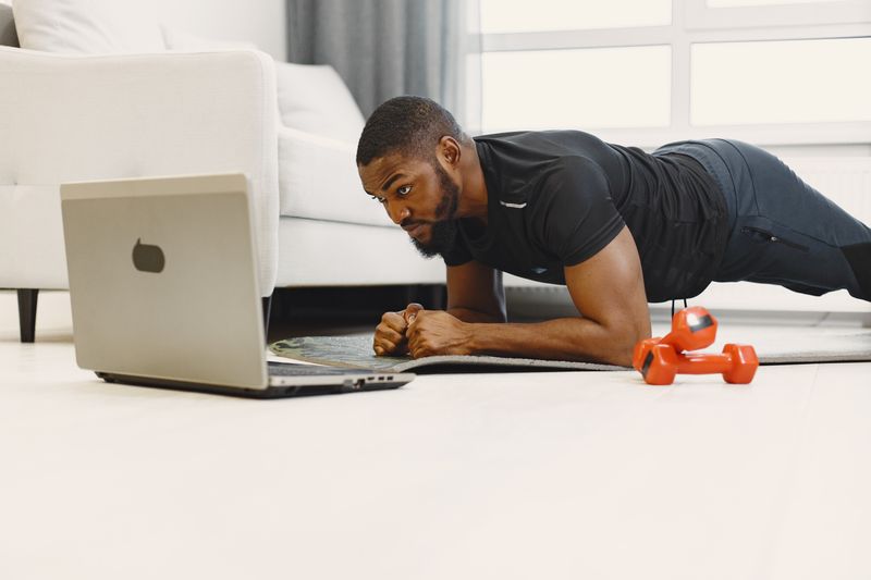 Homme en position de planche à la maison, suivant une séance sur son ordinateur portable